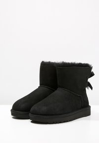 Bottines en suede noir avec une doublure en fourrure douce. Elles sont dotées d'une semelle en caoutchouc plate, d'un bout arrondi et d'un petit nœud à l'arrière.
