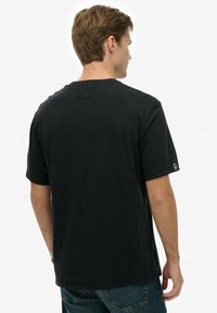 Camiseta negra de manga corta hecha de algodón suave, diseño de cuello redondo, ajuste ligeramente relajado, con una pequeña etiqueta de logo en la manga izquierda.