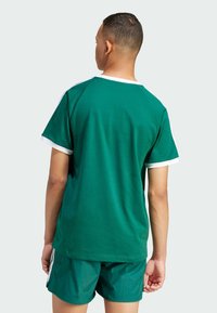Green cotton t-shirt with white accents, short sleeves, and a relaxed fit, paired with matching green shorts. Smooth texture, minimal design.