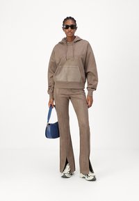 Sudadera con capucha de ante marrón con bolsillo frontal, combinada con pantalones acampanados a juego que presentan aberturas laterales. Incluye un bolso azul.