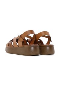 Sandal de color marrón con un diseño de tejido texturizado, que presenta correas anchas, hebilla ajustable y una suela de plataforma elevada con estrías horizontales.
