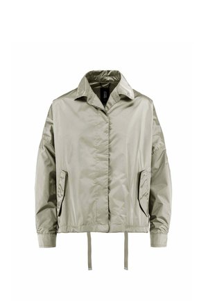 Jasnobeżowa, nylonowa kurtka z długim rękawem, kołnierzem, przednimi kieszeniami, elastycznym pasem i troczkami, pokazana na białym tle.