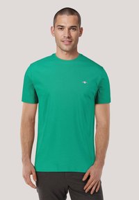 Grünes Baumwoll-T-Shirt mit Rundhalsausschnitt, kurzen Ärmeln und kleinem Logo auf der linken Brust. Glatte Textur, lässige Passform.