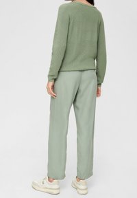 Maglione verde a maglia con maniche lunghe, abbinato a pantaloni leggeri verdi e sneakers beige, visto da dietro.