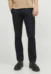 Navy blue pants in a slim fit, made of smooth fabric with front pockets and a flat front design. Paired with black loafers.