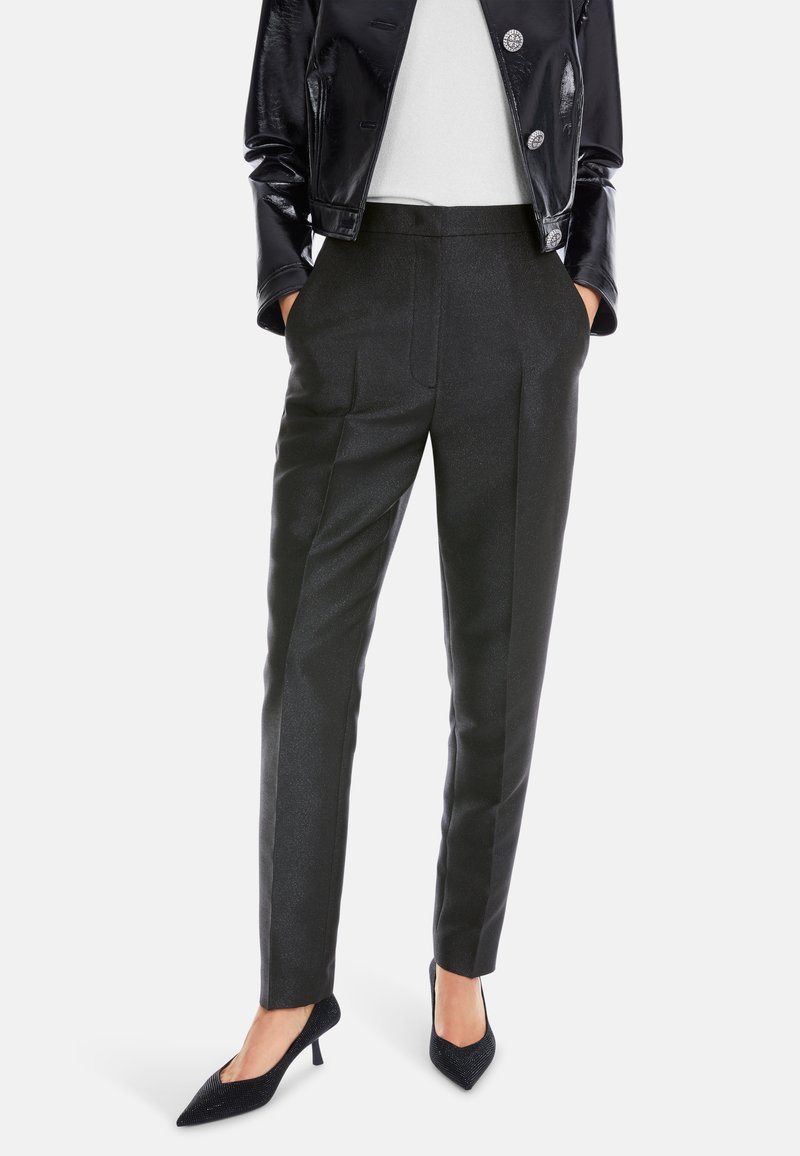 Schwarze maßgeschneiderte Hosen mit dezentem Glanz, gerade geschnitten und mit vorderen Falten. Kombiniert mit schwarzen spitzen Absätzen und einer taillierten Lederjacke.