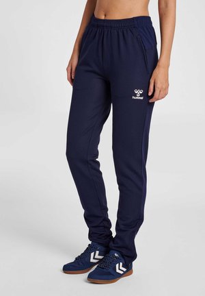 Person trägt dunkelblaue Slim-Fit-Jogginghose mit elastischem Bund und dazu passende dunkelblaue Sneakers mit weißem Chevron-Design.