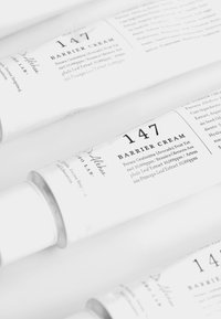 Barrierekremtube med en hvit matt overflate, svart tekst og en sølvfarge hette. Etikettene lister ingredienser og produktinformasjon tydelig.