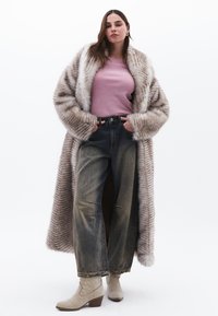 Langer, gestreifter Kunstpelzmantel in Beige und Braun, getragen über einem rosa Oberteil. Mit weitem, blassblauen Jeans und hellbeigen Stiefeletten.