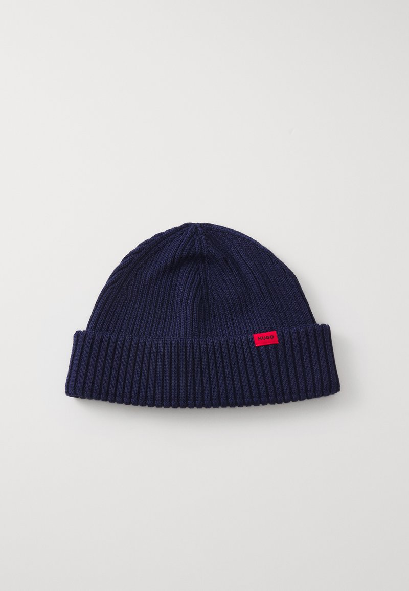 Gorro de punto azul marino con diseño de canalé, que presenta un puño doblado y una pequeña etiqueta de logo roja en el costado. Textura suave.