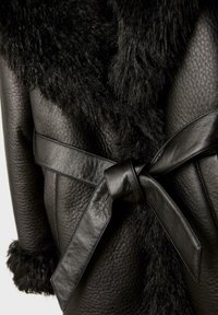 Czarna skórzana kurtka o teksturowanym wykończeniu, z kołnierzem i mankietami ozdobionymi futrem, zapinana na skórzany pasek wiązany w talii.