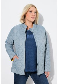 Chaqueta acolchada de color gris claro con cuello alto, cierre de cremallera y dos bolsillos laterales. Detalles amarillos en el cuello y acabado de tela texturizada.