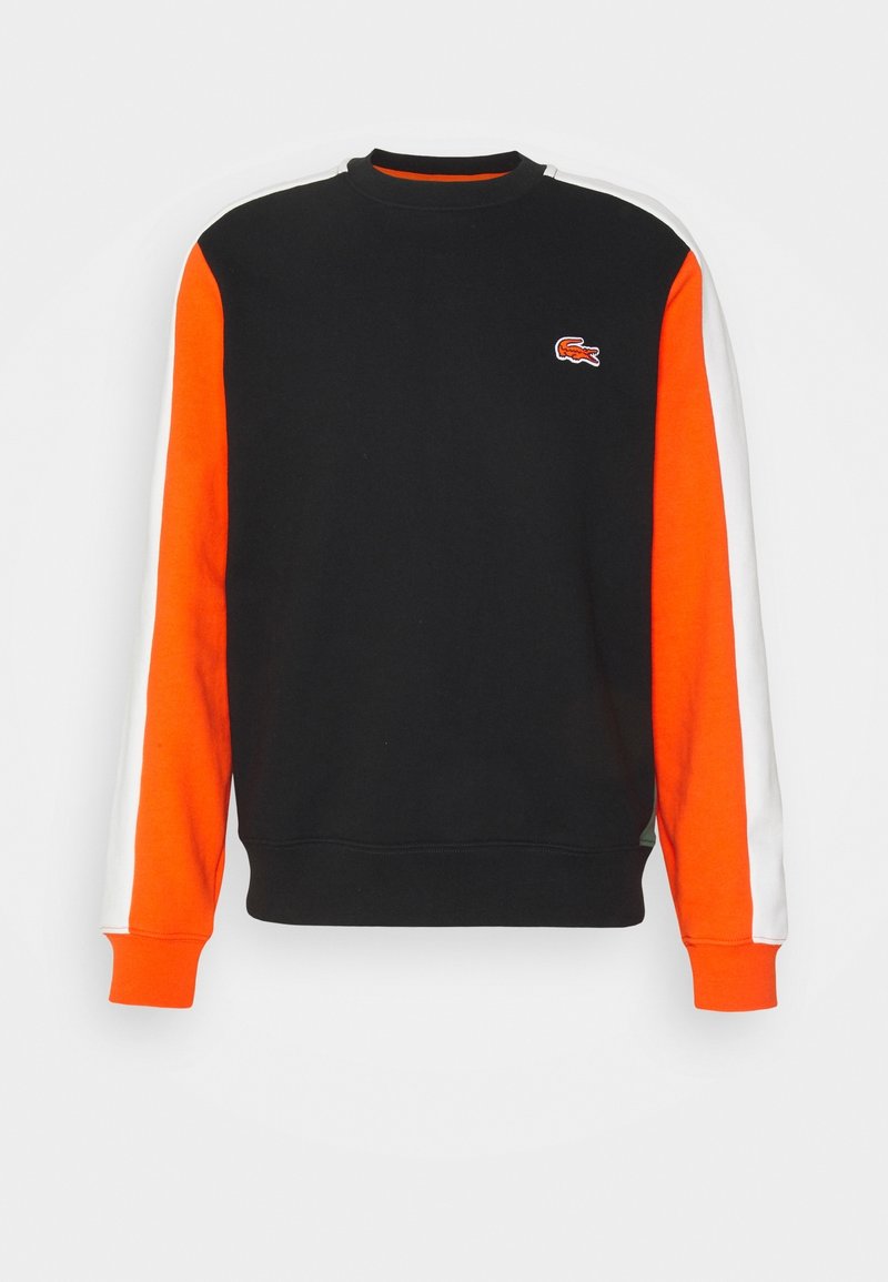 Sweat-shirt noir avec manches rayées orange et blanc et petit logo crocodile orange sur la poitrine gauche.