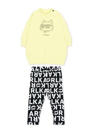 Geel sweatshirt met lange mouwen met opdruk van een kattengezicht en zonnebril, gecombineerd met zwarte leggings met witte letters en kattengezichtpatronen.