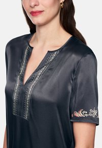 Dark satin blouse with a V-neck and short sleeves. Features detailed embroidery along the neckline and colorful accents on the sleeve.