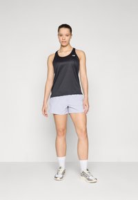 Svart trenings-topp i tank-stil kombinert med lysegrå shorts. Toppen har rund hals og logo-detaljer; shortsen har en løs passform og glatt tekstur.