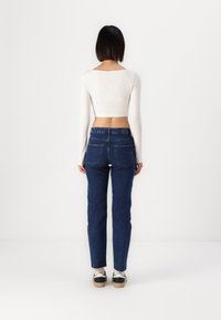 Top corto de manga larga blanco combinado con jeans de denim azul oscuro. Los jeans cuentan con dos bolsillos traseros y un logo sutil encima de la cinturilla.