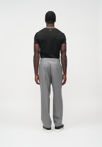 Czarny dopasowany t-shirt o prostym wzorze, zestawiony z jasnoszarymi, dopasowanymi spodniami z tylnymi kieszeniami i prostymi nogawkami, noszony z czarnymi trampkami.