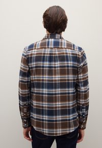 Camicia a quadri marrone e blu con colletto abbottonato, maniche lunghe e orlo curvo. Realizzata in tessuto morbido e strutturato con motivo a quadretti.