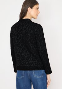 Zwarte jas met luipaardprint gemaakt van gestructureerde stof, voorzien van een geribbelde kraag en manchetten. Draagt een casual ontwerp met blauwe spijkerbroek.