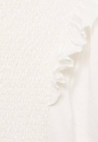 Biely textil so smockovanou textúrovanou panelou a volánikovým detailom pozdĺž švu odevu.