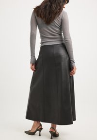 Gonna maxi in pelle nera con texture liscia, cuciture laterali e silhouette svasata, abbinata a un top a maniche lunghe aderente grigio a costine.