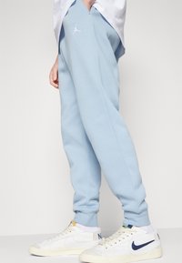 Světle modré tepláky s manžetami na nohavicích, se znakem Jumpman v bílé barvě. Nosené s bílými teniskami a světlou košilí navršenou nahoře.
