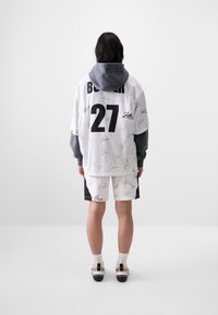 White jersey with black accents and signatures, gray hood, matching shorts with black side panels, and black sandals with white text.