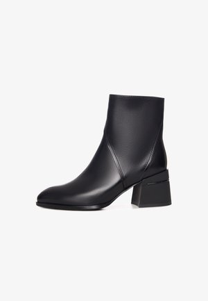 Zwarte enkelboot van glad leer met een puntige neus, voorzien van een blokhak en een minimalistisch ontwerp. Geen zichtbare patronen of hardware.