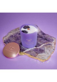 Świeca lawendowa w matowym, fioletowym szkle, ozdobiona kamieniami i drewnianym knotem, umieszczona na wypolerowanej płycie ametystowej. Różowa pokrywka.