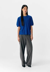 Blauwe textuurblouse met korte pofmouwen, gecombineerd met grijze wijde broek. De blouse heeft een subtiel geometrisch patroon en een ronde halslijn.