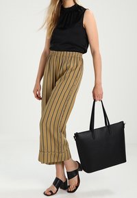 Černý top bez rukávů s nařaseným výstřihem, tanové pruhované široké kalhoty, černá taška přes rameno a černé sandály se širokými pásky.