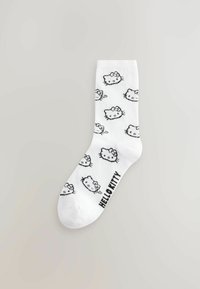 Witte katoenen sok met zwarte Hello Kitty-cartoongezichten, voorzien van een strik, en "HELLO KITTY" gedrukt aan de onderkant in vetgedrukte zwarte tekst.
