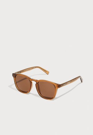 Gafas de sol cuadradas marrones con montura transparente naranja. Lentes marrones oscuros, varillas delgadas con detalles del logo en plata.
