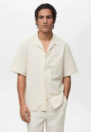 Short-sleeve, light beige shirt made of a textured fabric. Features a notch collar, front pocket, and button closure.