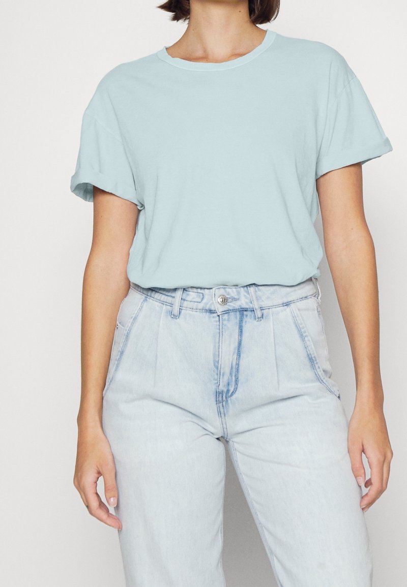 T-shirt bleu clair à col rond en tissu doux, avec des manches courtes retournées, associé à un jean en denim clair à taille haute.