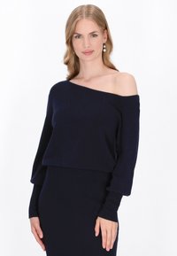 Pulover bleu marin cu umeri descoperiți, confectionat dintr-un material tricotat moale, având mâneci lungi și un design scurt. Textură netedă cu tiv ribatat.