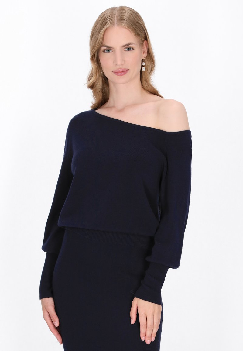 Pulover bleu marin cu umeri descoperiți, confectionat dintr-un material tricotat moale, având mâneci lungi și un design scurt. Textură netedă cu tiv ribatat.