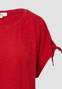 Rode t-shirt met korte mouwen, een ronde hals en geplooide details op de mouwen, gemaakt van een textuurstof. De silhouet heeft een relaxte pasvorm.