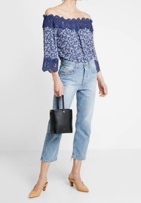 Marinblus med avskuren axel, blommönster och spetsdetaljer, i kombination med ljusblå jeans, svart handväska och nakenfärgade klackar.