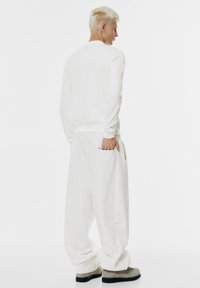 Weißes Langarmshirt mit rundem Halsausschnitt, kombiniert mit übergroßen hellgrauen Jogginghosen mit Seitentaschen und lockerem Schnitt.