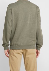 Sudadera de color verde oscuro con puños y dobladillo acanalados, tejido de mezcla de algodón, diseño de cuello redondo, llevada con pantalones caqui, mostrando vista posterior.