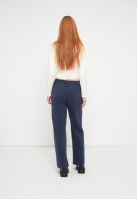 Mørkeblå joggingbukser lavet af blødt stof, med elastik i taljen og sidelommer, kombineret med en lys, strikket hvid cropped sweater.