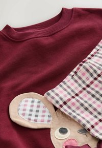 Bordeauxfarbenes Sweatshirt mit einem Mäusegesicht-Design, das beige und karierte Akzente aufweist. Weicher Stoff; runder Hals mit gerippten Abschlüssen.