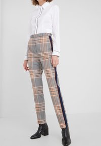 Pantalons à carreaux gris avec des accents orange et bleu, dotés d'une taille élastique et de bandes latérales. Associés à une chemise blanche avec des finitions noires.