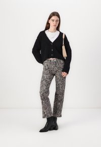 Cardigan nero, lavorato a maglia spessa con grandi bottoni, abbinato a pantaloni in stampa pitonata e stivaletti neri. Mini borsa con una tracolla come accento.