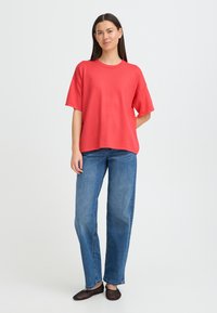 T-shirt surdimensionné corail avec encolure ronde, associé à un jean droit bleu et des chaussures plates noires. Texture lisse, design décontracté.