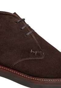 Bottine montante marron en daim pour homme, à lacets, avec des coutures détaillées et une semelle foncée, montrée en gros plan.