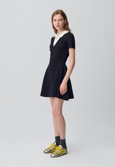 Vestito navy a maniche corte con colletto bianco a contrasto, gonna svasata, abbinato a sneakers argentate e gialle e calzettoni grigi.
