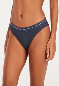 Tamsiai mėlynas bikini apatinis trikotažas su tekstūruotu audiniu, turintis spalvingą geometrinį raštą ant liemens. Žemas juosmens dizainas ir minimalus uždengimas.